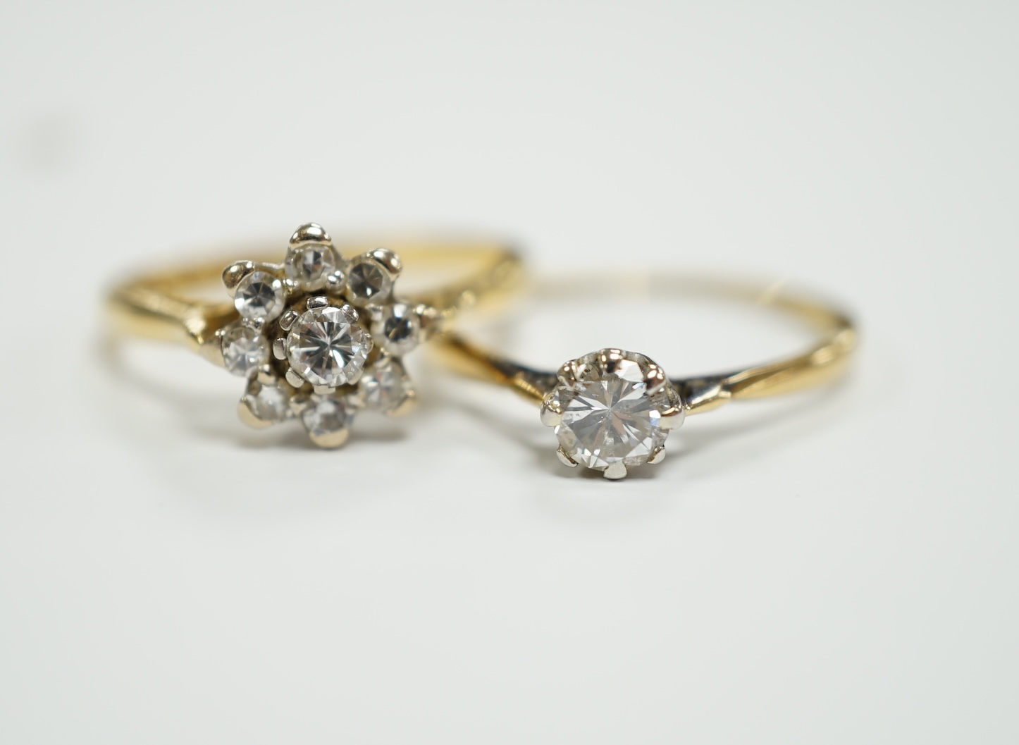 An 18ct gold and diamond cluster set flower head cluster ring, size K and an 18ct, plat. and solitaire diamond set ring, size L, gross weight 4.3 grams.